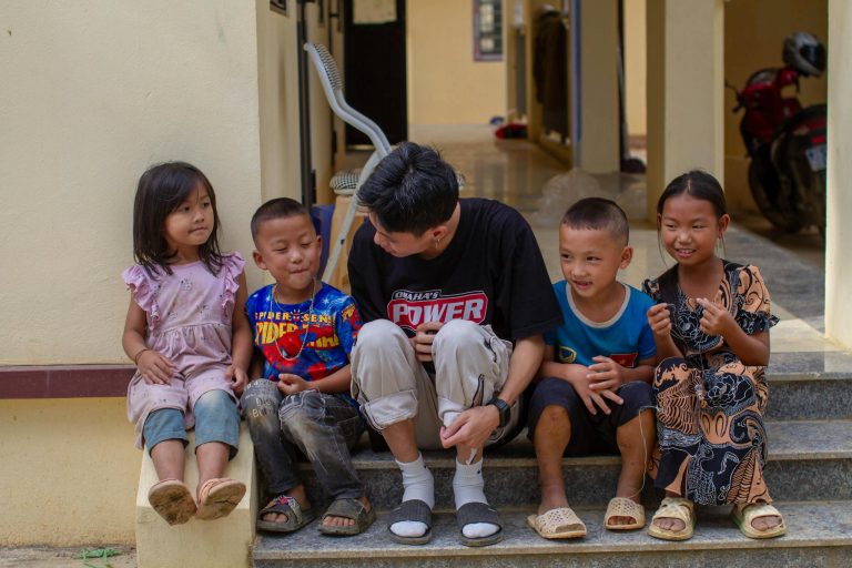 Five children and an adult sitting on outdoor steps, smiling and interacting.