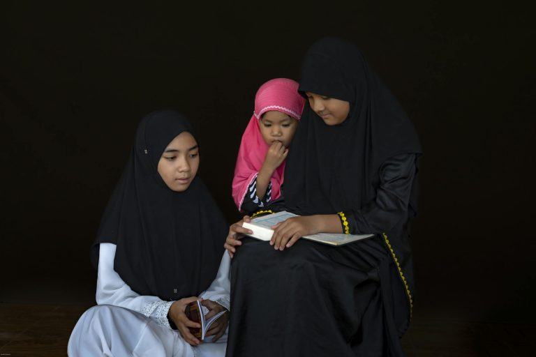 Three young girls in traditional attire read together, fostering knowledge and cultural connection.
